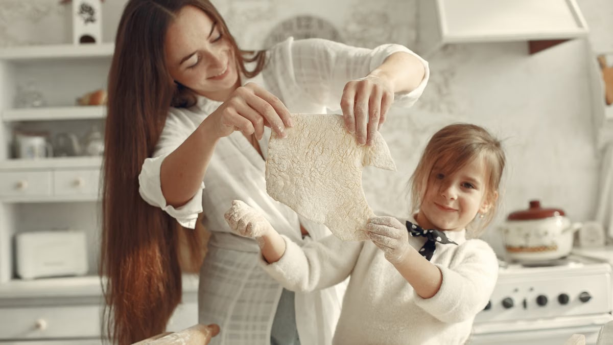 A mother and daughter joyfully preparing dough in a cozy kitchen setting.